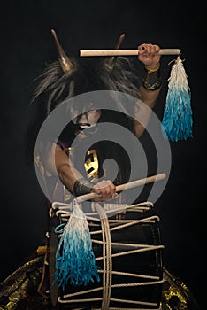 Demon from Japanese mythology. Portrait of an artist drummer Taiko in a wig with horns and demonic make-up drum on stage