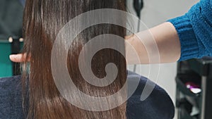 Demonstration of smooth and silky brunette hair after straightening and keratin treatment. Hairdresser shows a lock of