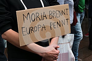 Demonstrator holds a cardboard sign with German text Moria brennt, Europa pennt, meaning Moria is burning, Europe is sleeping, on