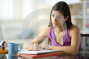 Demotivated and worried student taking notes looking away