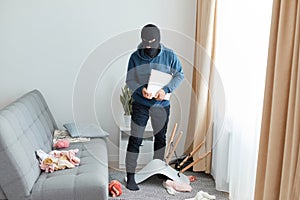 Dengerous man in a black mask and blue hoodie enters someone else`s house to rob the owners, breaking apartment for stealing