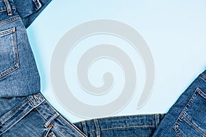 Denim background. Pile of blue jeans on light blue background. Variety of casual trousers and clothes. Top view to frame