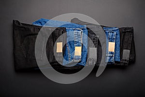Denim blue jeans and black jean stacked in pile on black background Top view. Denim jean pants wear folded in stack.