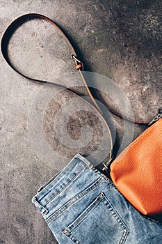 Denim blue jeans stacked and brown leather cross body bag on a dark textured rustic background. Fashionable casual outfit. Top