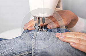 Denim clothing on sewing machine close up, male hands