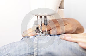 Denim clothing on sewing machine close up, male hands