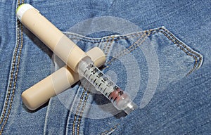 On the denim fabric, an insulin pen for injections of a patient with diabetes mellitus. the concept of the disease of young people