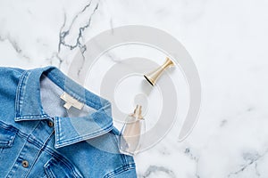 Denim jacket and bottle of perfume on marble background. Flat lay design composition with feminine clothing and accessories. Beaut