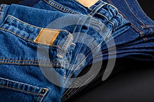 Denim jean pants folded in stack with empty brown tag mockup label. Casual wear blue jeans stacked in pile on black