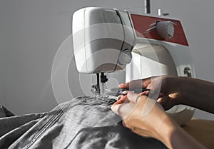Denim jeans cloth on sewing machine closeup. Women hands at manual work