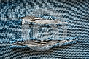 Denim jeans texture background for design. Hole and threads on old Jeans material
