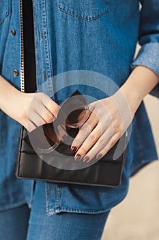 Denim outfit fashion details. Stylish woman with red glitter manicure in navy jeans holding sunglasses and leather small cross bod