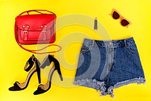 Denim shorts, black shoes, red handbag and glasses. Bright yellow background. Fashionable concept