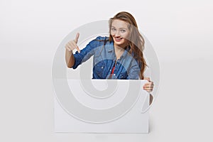 Denim style portrait of teen girl on the floor holding white blank advertising board banner, over white background