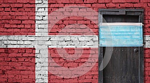 Denmark flag painted on brick wall and closed door with medical mask protected