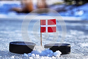 Dánska vlajka na špáradlo medzi dvoma hokejovými pukmi. Dánsko bude hrať na Svetovom pohári v skupine A. 2019 IIHF World Championship