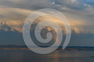 Dense clousd above lake with rainbow