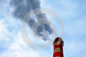 Dense emissions into the atmosphere of industrial waste from the factory pipe, against the blue sky