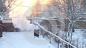 Dense smoke from burning garbage in an iron barrel against the backdrop of a winter suburban landscape. Sunset through trees and f