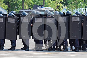 Dense system of police with metal armored boards before soldiers. Police officers keep a system in helmets, heavy army boots,