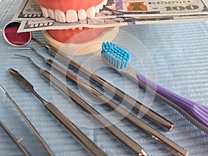 Dental artificial jaw instrument and hundred dollar bills on table at dentist