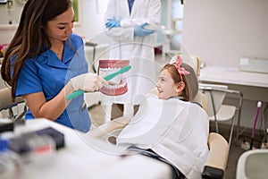 Dental assistant showing to child how to brushing her teeth