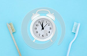 Dental care. Dental hygiene and treatment. Alarm clock, toothbrushes on light blue background. Healthy teeth. Morning routine