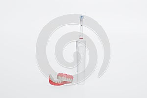 Dental care with an electric brush. Dentures and an electric brush on a white background. Acrylic dentures. Oral hygiene.