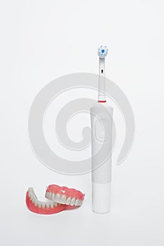Dental care with an electric brush. Dentures and an electric brush on a white background. Acrylic dentures. Oral hygiene.