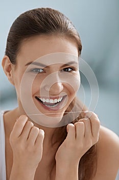 Dental care. Smiling woman cleaning white teeth with floss