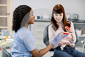 Dental care and teeth hygiene. Young smiling African american female dentist showing teeth and jaw model to her pretty