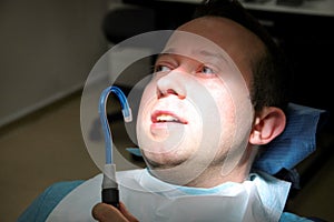 Dental check up. Dental male patient at regular dental check, at dental clinic and office. Man with dental suction tube in mouth.