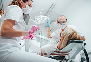 Dental clinic patient appointment. Dentist man in magnifying glasses pointing light. Young female assistant ready for teeth