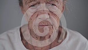 Dental concept. Elderly female 90 years old inserts denture. Senior woman gray hair using dental prosthesis on gray