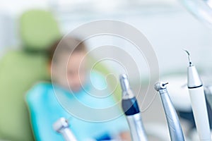 Dental drills and tools in dentist`s office. In the background, an unrecognizable patient in a dental chair. Blurry