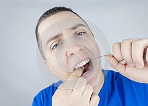 Dental floss close up. A man in front of a mirror brushes his teeth with flossing. The concept of proper oral care. Selective