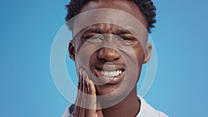 Dental health problem. Young african american man massaging his painful jaw, suffering from toothache, blue background