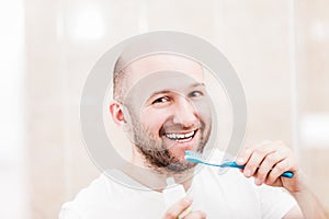 Smiling bald man holding toothbrush with toothpaste and brushing teeth