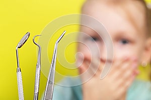 Dental instruments against the background of a frightened girl who covers her mouth with her hands. The concept of