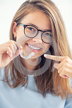 Dental invisible braces or silicone trainer in the hands of a young smiling girl. Orthodontic concept - Invisalign