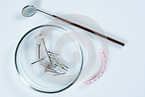 Dental medical tools, dentist equipment: false teeth, stomatological mirror and used dental burs in Petri dish glass on light blue