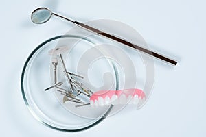 Dental medical tools, dentist equipment: stomatological mirror, false teeth and used dental burs in Petri dish glass on