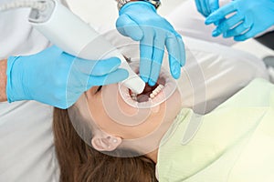 Dental practitioner examining oral cavity of woman supervised by nurse