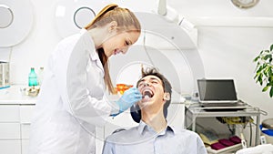 Dental professional checking overall oral health of young happy male patient sitting in chair