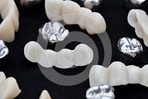 Dental silver metal tooth crowns and ceramic or zirconium tooth bridges on dark black surface. photo