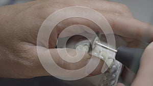 Dental technician holding artificial jaw mold with teeth and polishing them in the lab. Dentist brushing teeth with professional w