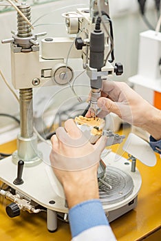 A dental technician makes partial dentures on a mechanized machine. The production of the false jaw or dental bridges