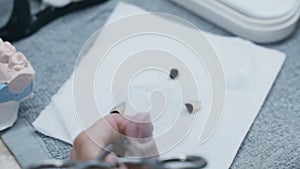 A dental technician paints a ceramic crown with a brush and dental paints.