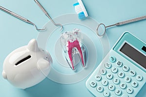 Dental tool and tooth with piggy bank and calculator on blue background