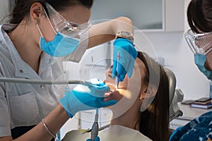 Dentist with assistan treats teeth to a girl in a clinic